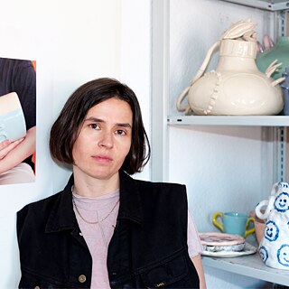 Forfatteren Clara Umbach sidder ved siden af en reol med keramik.