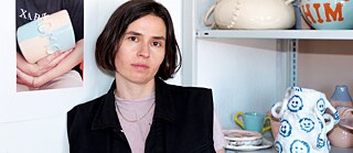 Forfatteren Clara Umbach sidder ved siden af en reol med keramik.