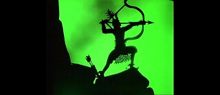 Scherenschnittbild, das die Silhouette eines Bogenschützen vor grünem Hintergrund zeigt