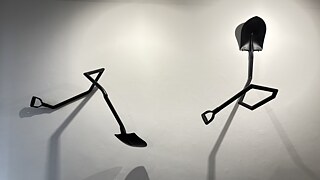 Wall-mounted sculptural installation made from black metal shovel and spade components arranged in abstract, geometric forms against a white gallery wall at the Goethe-Institut Johannesburg exhibition A Secret Third Thing.