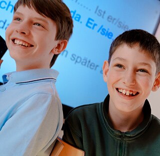Zwei Schüler sitzen vor einem Bildschirm mit deutschem Unterrichtsmaterial und nehmen an einer Deutschstunde teil.
