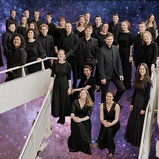 Choir ensemble in black concert attire standing on a staircase and platform beneath a star-filled dome projection at the Wits Anglo American Digital Dome.