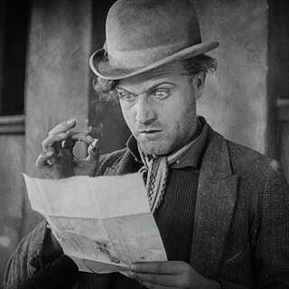 Historisches Schwarz-weiß-Standbild aus einem Stummfilm. Eine Person mit Melone, Jackett und Halstuch hält ein gefaltetes Blatt Papier in den Händen. Im Hintergrund sind Gebäudesäulen zu sehen.