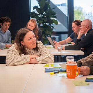 People collaborating and talking around tables in a bright workshop or meeting room.