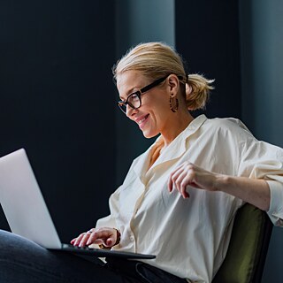 Eine Frau arbeitet am Laptop. Sie sitzt entspannt auf einem Sessel und nimmt an einem Videocall teil.