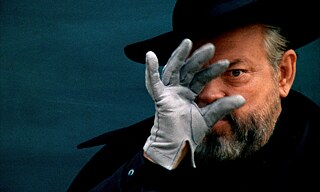 Un uomo con barba grigia, un cappello nero e una mano guantata che gli copre gran parte del viso