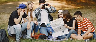 Skupina přátel, kteří sedí na trávě a prohlížejí si mapu.