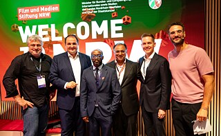 Group photo at Games Connect Africa at the Film und Medien Stiftung NRW stand, with six participants posing in front of a “Welcome to NRW” display.