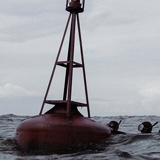 Scena tratta dal film Jenseits der blauen Grenze: due nuotatori in muta e maschera si aggrappano a una boa di delimitazione marittima nel Mar Baltico.