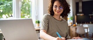 Frau schaut lächelnd auf einen Laptop, während sie Deutsch lernt