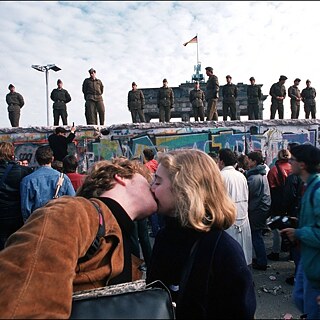 Ein Pärchen steht vor der Berliner Mauer und küsst sich.