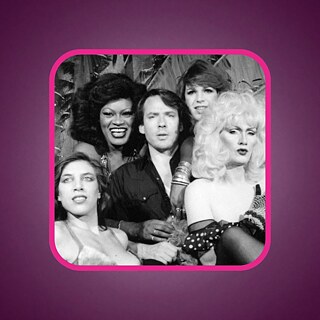 Black-and-white photograph of five people posing closely together in an ornate nightclub interior, wearing theatrical clothing, hairstyles and accessories. The image is framed by a thick, rounded bright pink border.