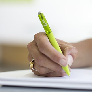 A female hand writes on a notepad using a green Goethe-Institut pen.