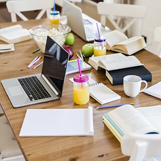 Auf dem Tisch liegen diverse Arbeitsmittel, Laptops, Bücher, Schreibblöcke, Bücher und Stifte sowie Getränke, Popcorn und Äpfel.