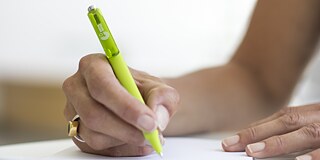 A female hand writes on a notepad using a green Goethe-Institut pen.