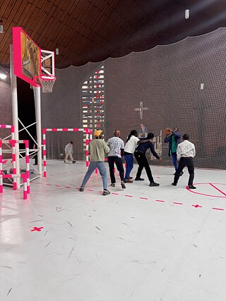 Mehrere Besucher spielen in einer künstlerisch gestalteten Indoor-Sportanlage mit Basketballkorb und Fußballtor.