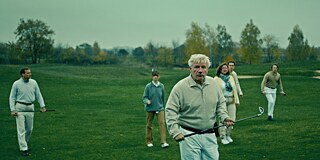 escena de la película WIR KÖNNTEN GENAUSO GUT TOT SEIN Grupo de personas caminando en un campo con palos de golf en las manos