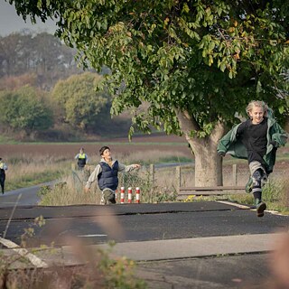 Two children are running along a country road; they are being chased by police officers.