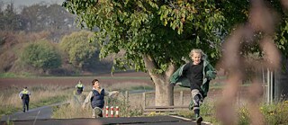 Two children are running along a country road; they are being chased by police officers.