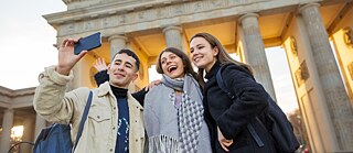 Drei Freunde machen ein Selfie vor dem Brandenburger Tor in Berlin.