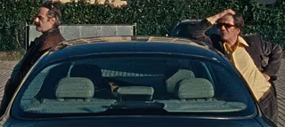 Zwei Männer, die an einem Auto lehnen.