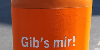 Ein orangener öffentlicher Mülleimer mit der Aufschrift "Gibs mir".