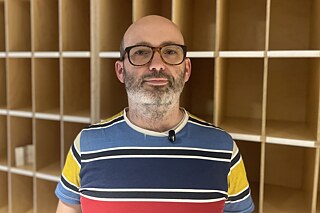Máté Halmos, Projektmanager des Socrates-Programms, vor einem hölzernen Fächerregal der CEU in Budapest. Früher hatte hier jede*r Studierende ein eigenes schmales Fach; einige Namen aus der Zeit vor dem Zwangsumzug nach Wien sind noch zu sehen.