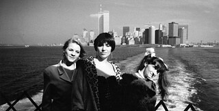 3 women are standing on a boat facing the camera. In the background the skyline of Manhattan with the World Trade Centre is visible.