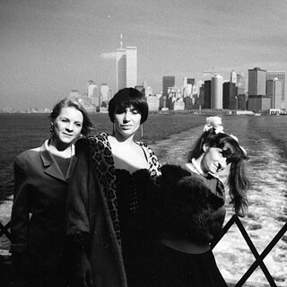 3 white women are standing on a boat facing the camera. In the background the skyline of Manhattan with the World Trade Centre is visible.