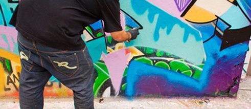 Ein Sprayer, der nicht abgebildet und auch nicht erkannt werden will, sprüht ein nicht genehmigtes Graffiti an eine Wand in Berlin