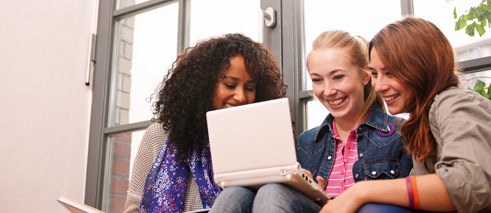 Drei Sprachschülerinnen schauen in einen Laptop.