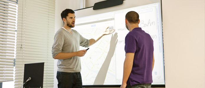 A teacher explaining something to a language student on an interactive whiteboard.