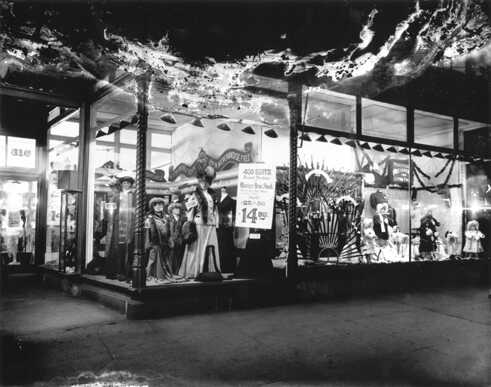 Shop Window, 816 7th Street NW, around 1907. The lights of these shop windows, perhaps readied for the holidays, entice you to consider a fur, a new suit (a steal, really, at $14.95), a new umbrella, or perhaps some 'Practical Presents for Little Folks'.