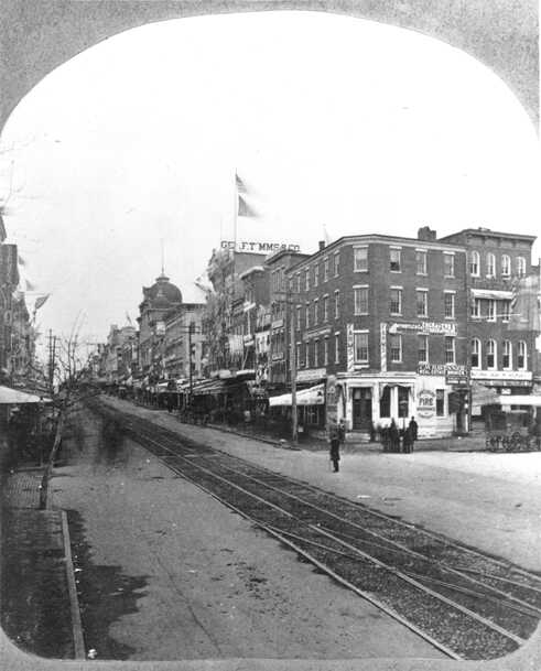 7th Street, östliche Seite, dekoriert für die Amtseinführung des Präsidenten James Garfield, 4. März, 1881. Der Washington Sängerbund war Teil des Umzugs während der Feierlichkeiten. Anders als die Gravur 1875 übermittelt diese Fotografie einen weniger eleganten, eher heruntergekommenen Eindruck des Lebens in der 7th Street. Am 2. Juli 1881, vier Monate nachdem dieses Foto entstanden ist, wurde President Garfield von einem Verwirrten an der Baltimore & Potomac Railroad Station angeschossen, das sich damals an Stelle des westlichen Gebäudes derNational Gallery of Art’s West Building befand. Garfield erlag seinen Wunden am 19. September.
