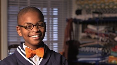 Young boy smiling into the camera. He is wearing a yellow bow tie.