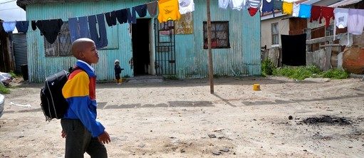 Scène du film « Pas sans nous », un petit écolier, cartable sur le dos, marche dans une rue du bidonville