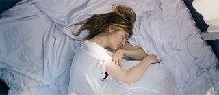 Scène du film. Les yeux fermés, une femme est allongée sur un lit. Elle enlace son enfant qui se cache sous sa chemise de nuit.