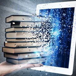 Eine Hand mit einem Bücherstapel vor einem Tablet