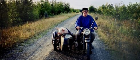 Die letzte Sau, Szenenbild: ein Mann fährt auf seinem Moped, im Beiwagen sitzt ein Schwein