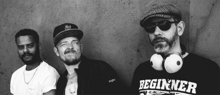 Die drei Musiker grinsend vor einer Wand