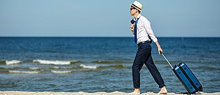 Mężczyzna spaceruje z walizką po plaży