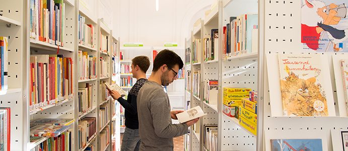 Zwei Männer blättern in Büchern zwischen Bücherregalen