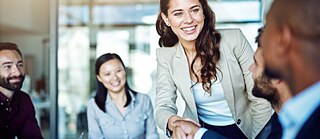 Eine Gruppe Personen in Businesskleidung. Eine junge Frau schüttelt einem Mann die Hand. 