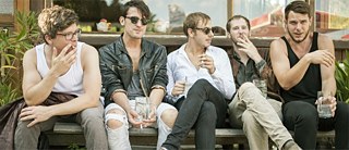 5 junge Männer auf der Bank sitzend, die trinken und rauchen