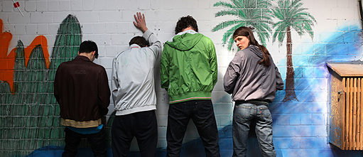 4 Personnes urinant contre un mur en briques décoré
