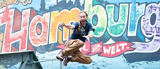 Mann springt vor einer Graffitiwand