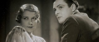 Un jeune homme aux cheveux foncés et une jeune femme blonde regardent au loin. Photo en noir et blanc