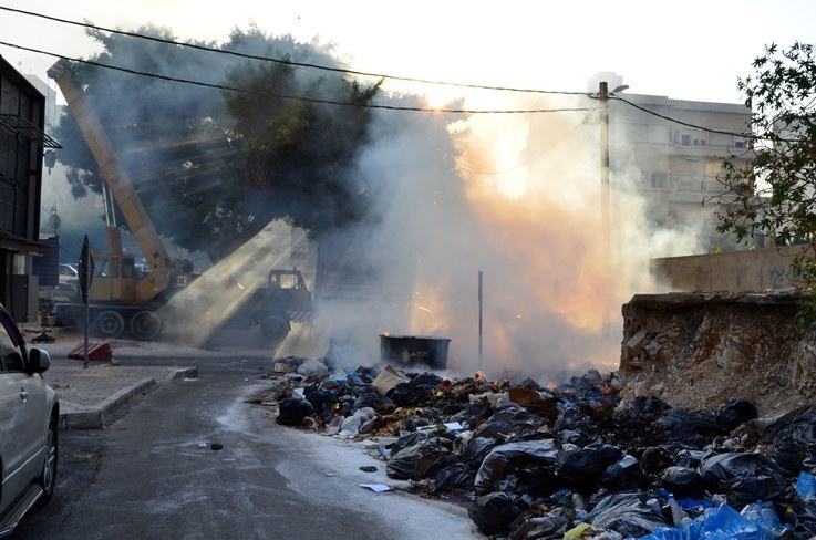 قمامة يتم حرقها وسط الشارع في بيروت. على اليمين كومة من أكياس القمامة، خلفها يرتفع لسان كبير من اللهب ودخان.