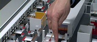 Menschen werden, wie Legos, in Miniatur, dargestellt und eine riesige Hand ragt von oberhalb hinein und zeigt auf sie