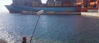 Mann sitzt am Meer und hält ein Mikro Richtung Container - Projekt Freiraum
